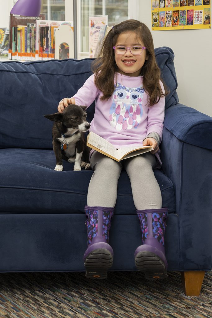 Young girl sitting with small dog as she reads a book in the children's reading area