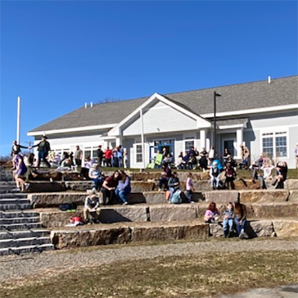 Families gathering in audience area of the outdoor amphitheater behind the library