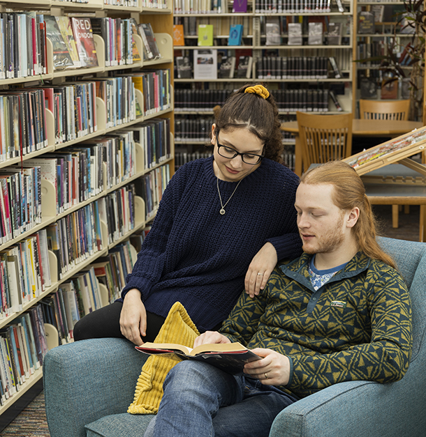 male reading book with female sitting next to him looking on